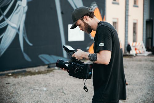 Free A man operating a professional video camera in an urban outdoor setting. Stock Photo