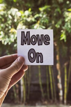 Hand holding a note with 'Move On' message against a bamboo background.