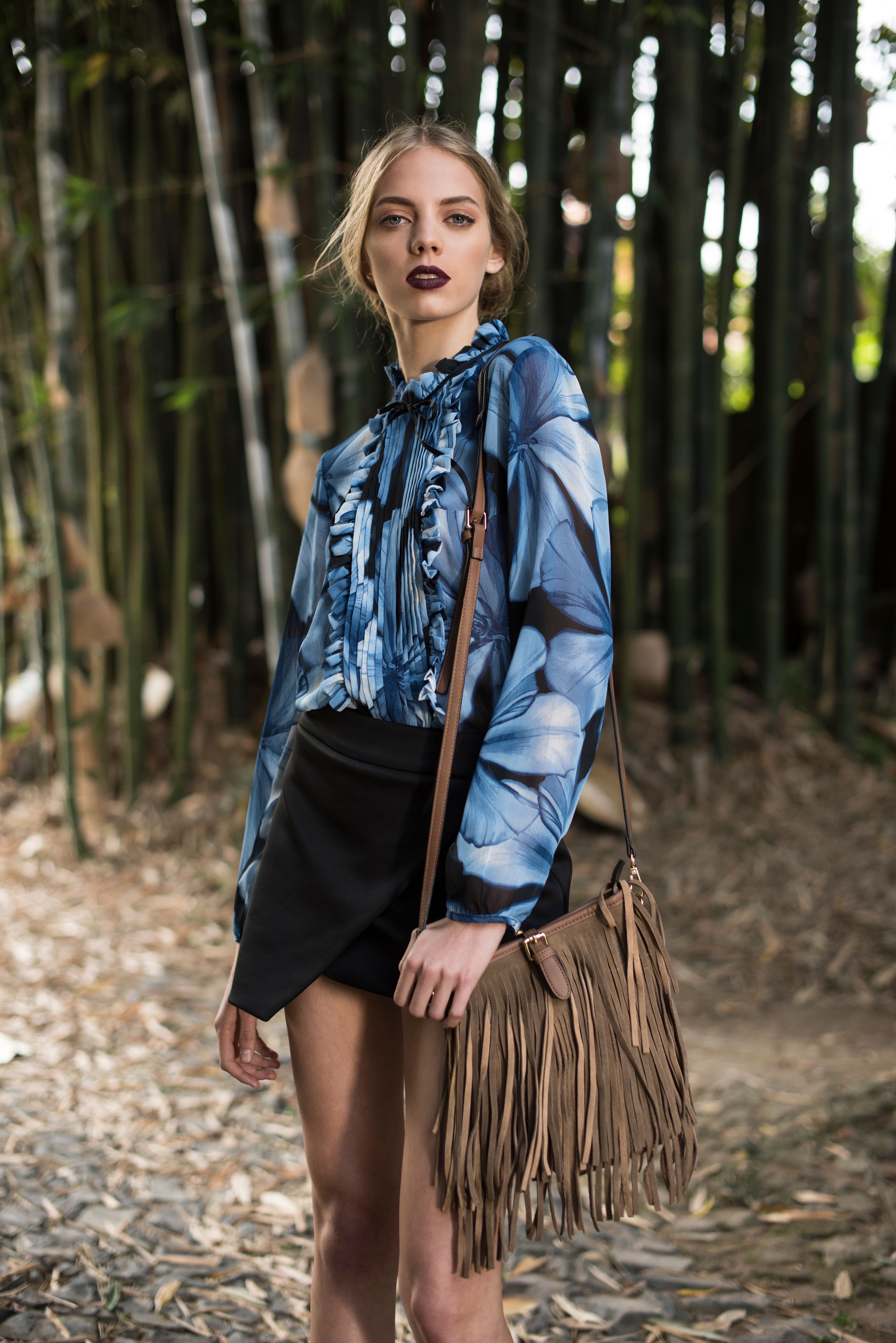 Modelo elegante exibindo estilo de moda com blusa floral azul em um cenário de floresta exuberante.