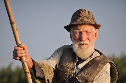Человек в шляпе держит деревянный стержень под серым небом
