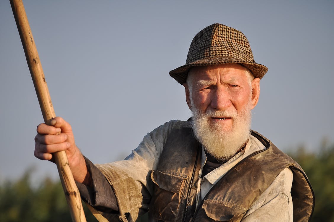 Man Wearing Hat Holding Wooden Rod Under Gray Sky