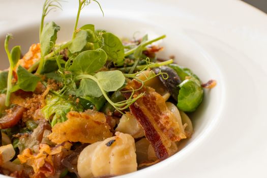 Delicious pasta dish garnished with fresh herbs, crispy bacon, and vegetables on a white plate.
