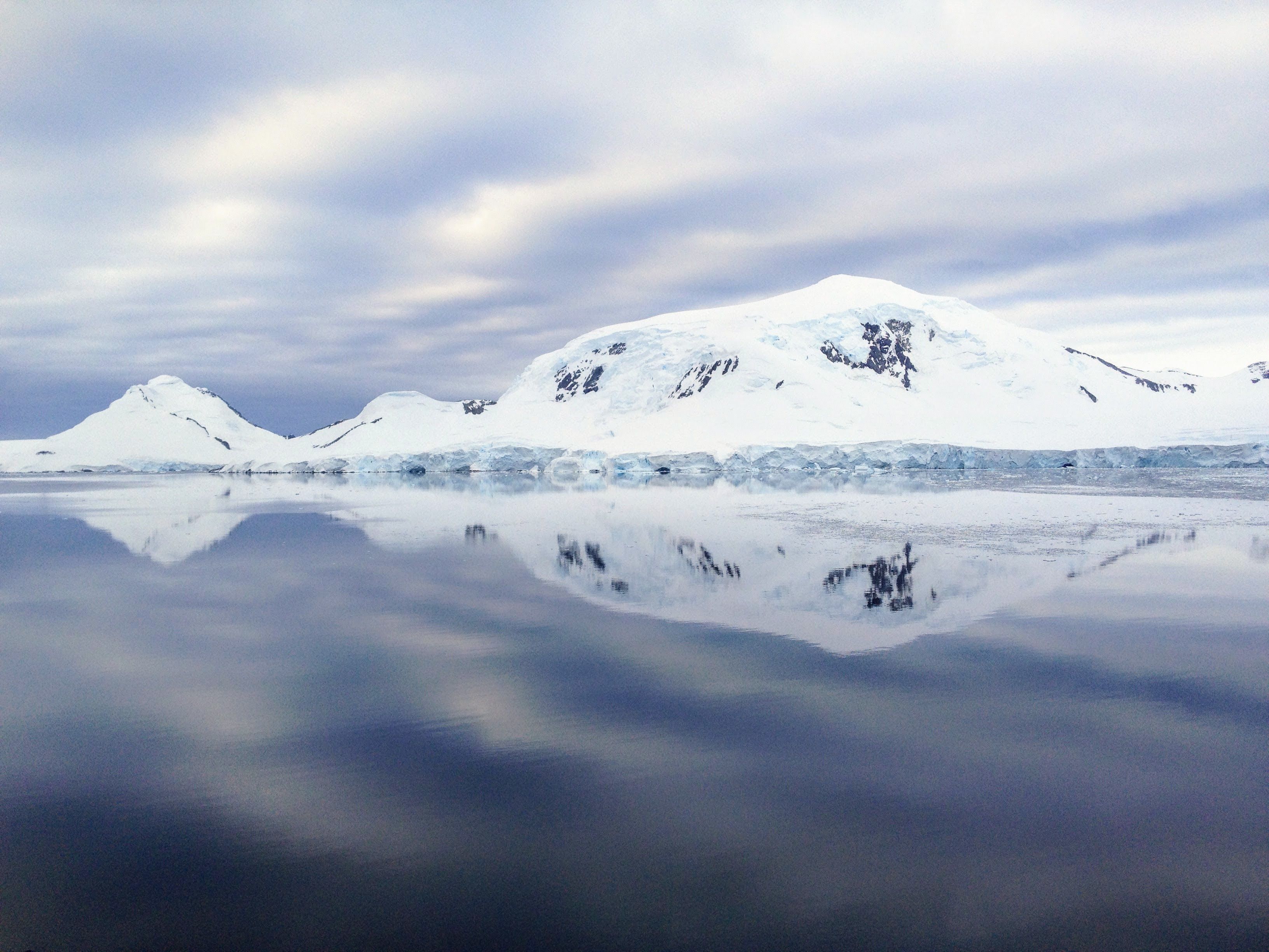 Snøkledte fjell speiler seg i det stille Polhavet ved Svalbard