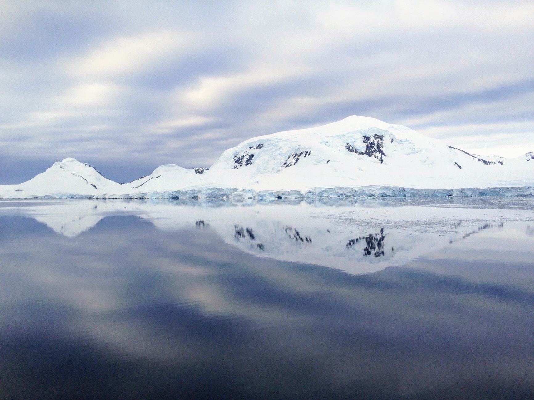 Snøkledte fjell speiler seg i det stille Polhavet ved Svalbard
