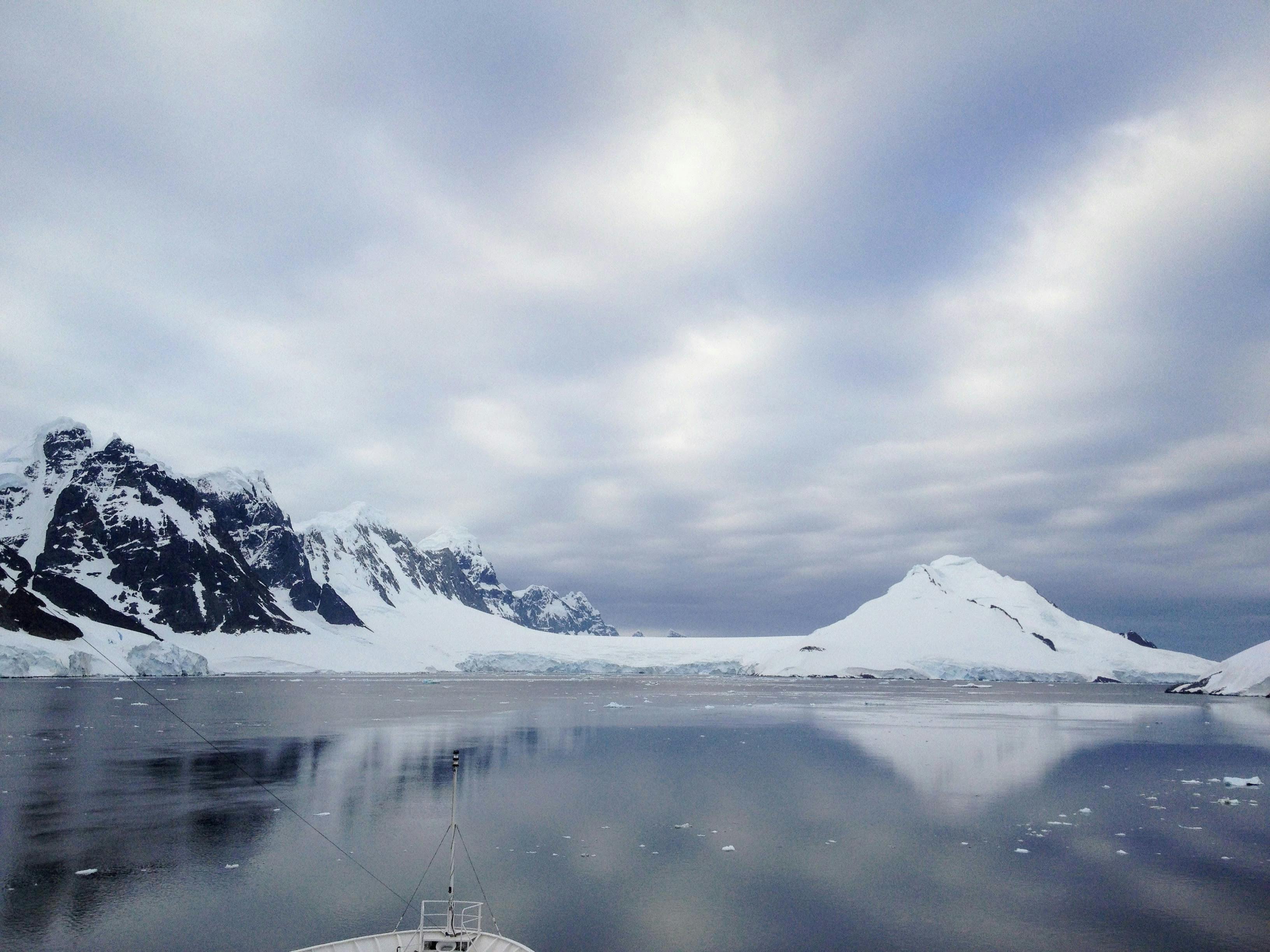 Serene landscape of snowy peaks reflecting on icy waters in Svalbard's serene wilderness.