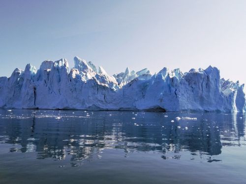 Free Massive iceberg in Greenland reflecting on the calm ocean water under a clear sky. Stock Photo