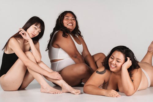 Free Happy Asian females with different figures types wearing lingerie and sitting on floor against white background Stock Photo