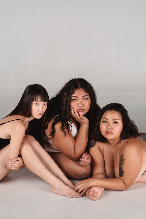 Emotionless Asian women in underwear sitting on floor in studio