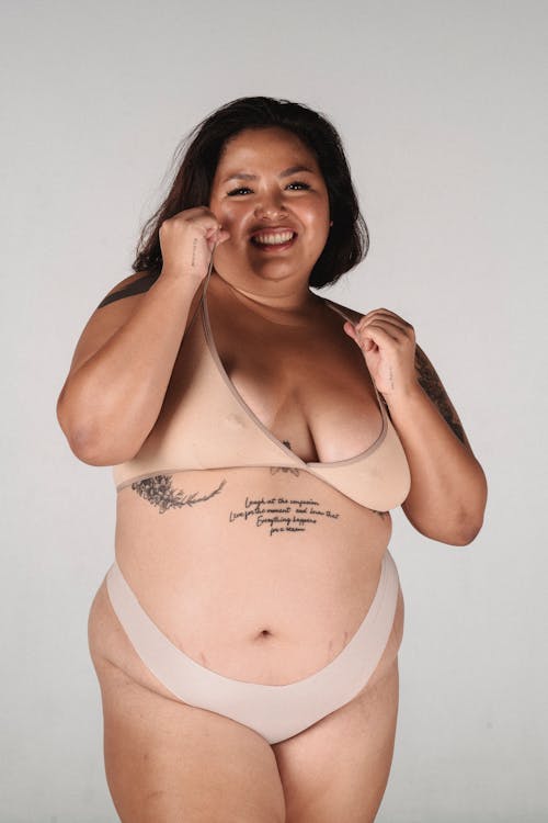 Happy plus size woman in lingerie smiling and standing in studio against gray background