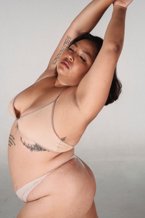 Free Tattooed Asian woman with short dark hair and closed eyes standing with raised arms in underwear in soft daylight Stock Photo