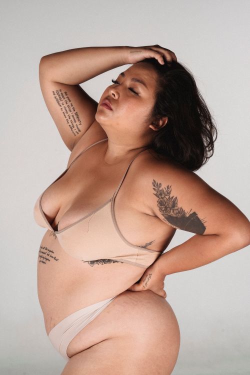 Free Side view of sensual Asian female in lingerie keeping eyes closed and touching hair and hip while standing against gray background Stock Photo