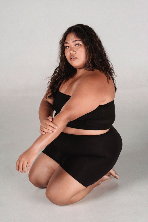 Free Full bode of plus size serious Asian female wearing black skirt and top looking at camera while sitting on white background Stock Photo
