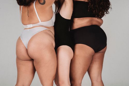 Free Back view of skinny female standing between plus size women in white and black underwear on white background in studio Stock Photo