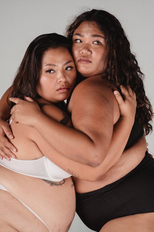 Calm plump Asian women in underwear embracing each other