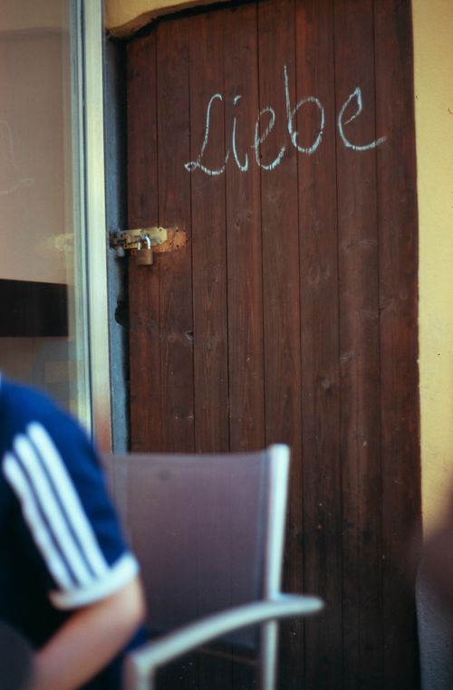 Free A rustic wooden door with the word 'Liebe' chalked on it, accompanied by a locked padlock. Stock Photo
