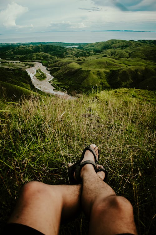 A Person Sitting on a Grass Field with Overlooking View of Green Hills