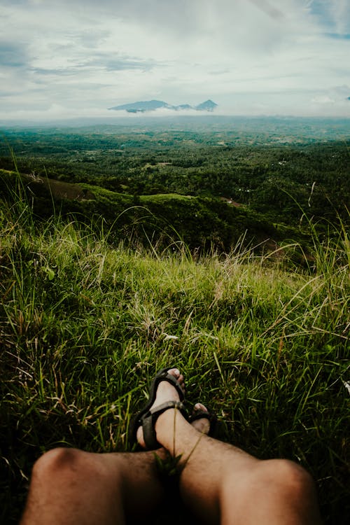 A Person Wearing Black Hiking Sandals Sitting on a Grass Field in front of a Beautiful View