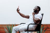 一个穿着白衬衫的男人正开心地坐在户外，用智能手机进行视频通话