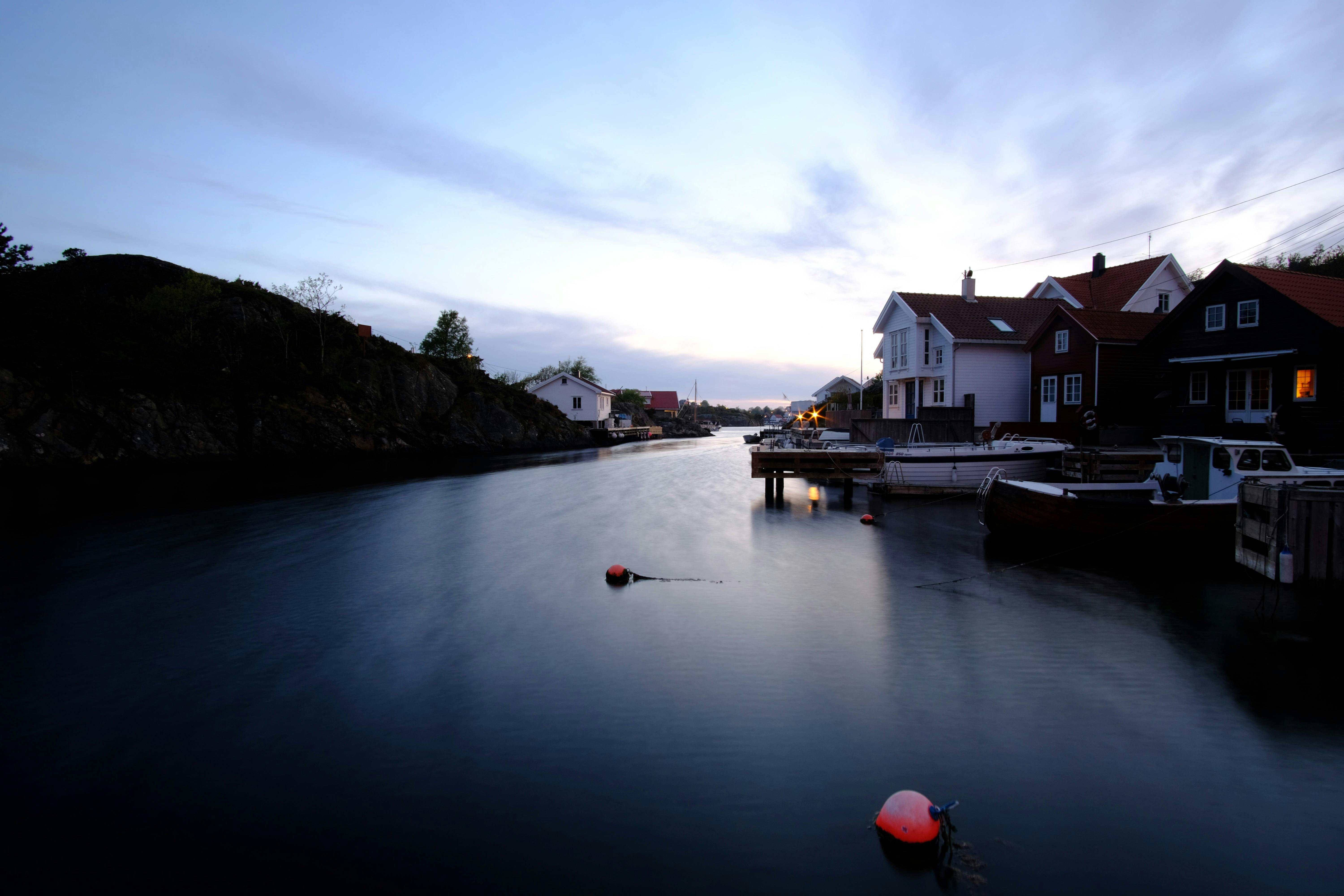 黄昏时分，宁静的海滨场景中，船只、房屋和倒映的水面在如画的天空下构成一幅画卷