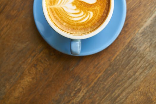 Top view of a cappuccino with intricate latte art in a blue mug on a wooden table.