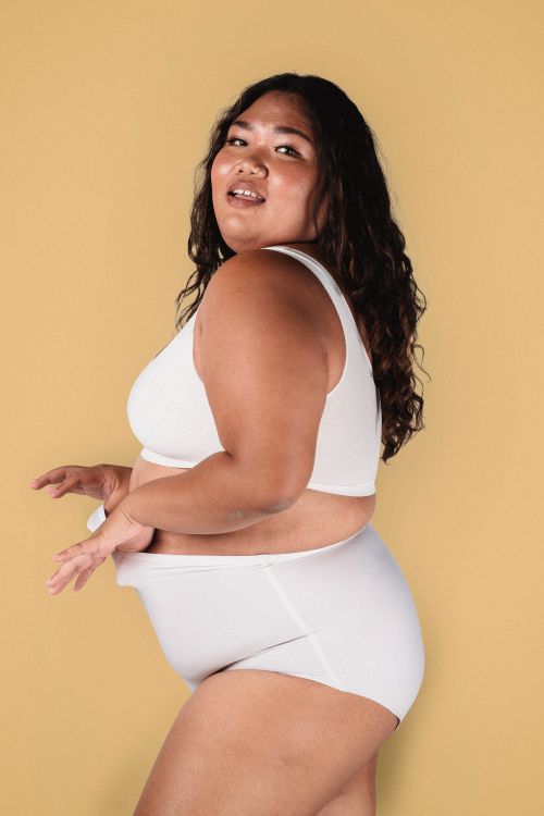 Free Side view of confident overweight female model in bra and panties standing against beige background and looking at camera Stock Photo