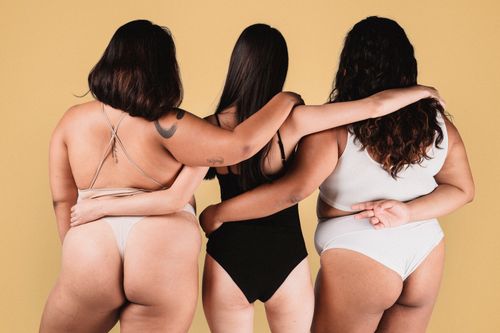 Free Back view of faceless female models in underwear hugging each other against beige wall in studio Stock Photo