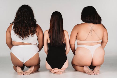 Free Back view of anonymous female models in lingerie sitting on floor against white wall in studio Stock Photo