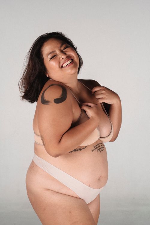 Free Side view of plus size female model in underwear holding hands on chest while toothy smiling against white background in studio Stock Photo