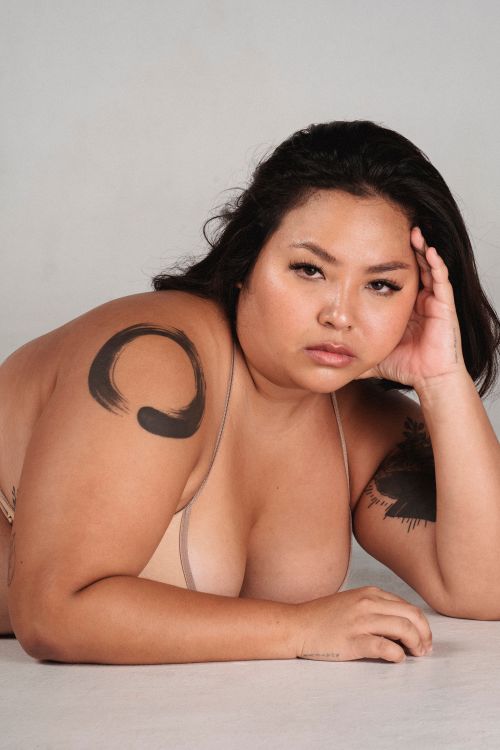 Free Confident Asian alluring young plus size woman leaning on hand while lying on floor in studio and looking at camera Stock Photo