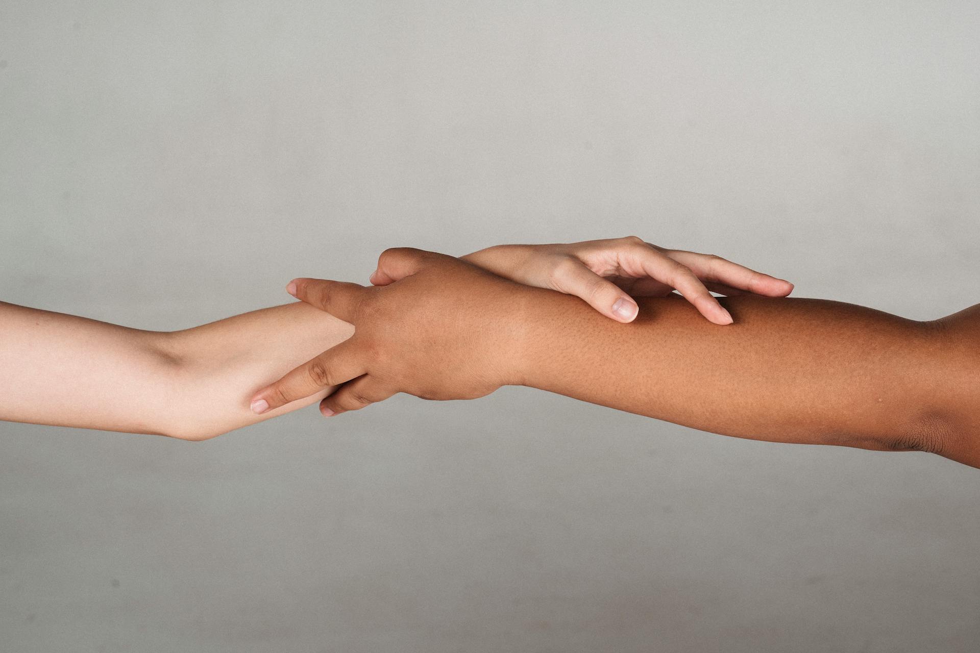 Crop anonymous multiracial female demonstrating unity and tolerance while reaching hands to each other in studio against gray background