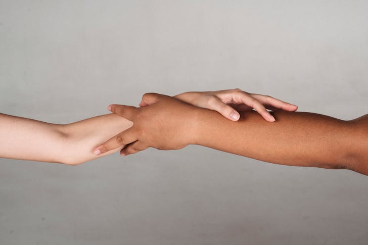 Crop anonymous multiracial female demonstrating unity and tolerance while reaching hands to each other in studio against gray background