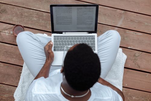 Free Man sitting outdoors on wooden deck using laptop, enjoying casual work setting. Stock Photo