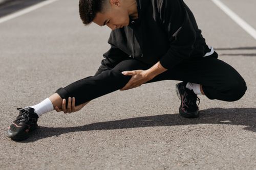 Free A young man performs stretching exercises on a city street, focusing on flexibility and fitness. Stock Photo