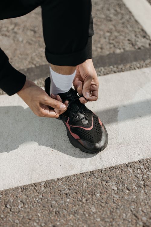 Free Close-up of a man tying black athletic sneakers on a road with white markings. Stock Photo