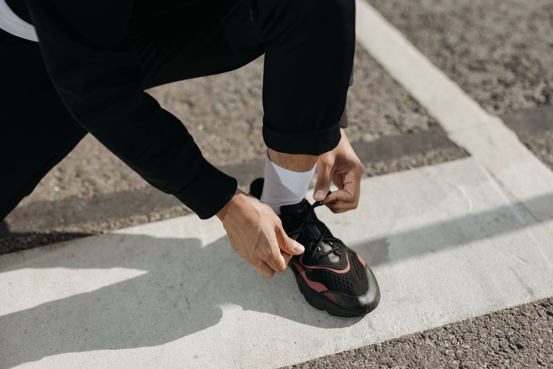 A Person Wearing Black Pants Tying the Lace of the Sneaker he is Wearing