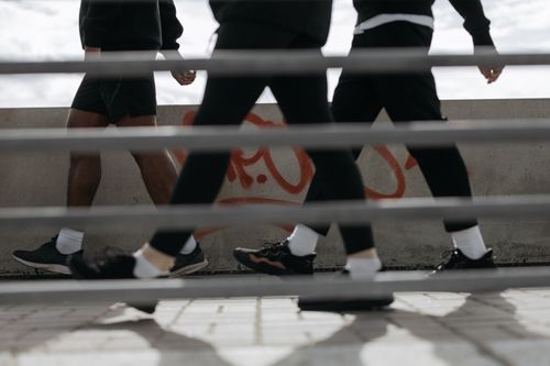 Free Low angle view of three people walking past a graffiti-covered wall, captured through bars. Stock Photo