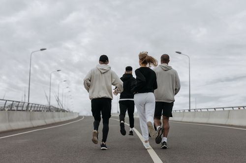 Free Four adults in athletic wear jogging together on an empty road under a cloudy sky. Stock Photo
