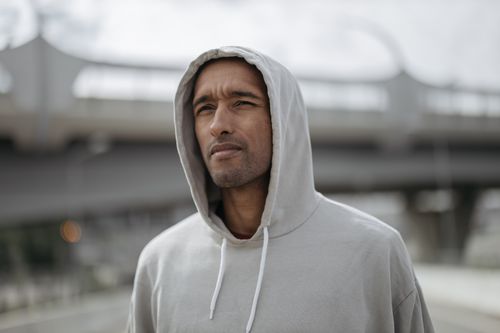 Free Close-up of a man in a gray hoodie, looking thoughtful outdoors in urban area. Stock Photo
