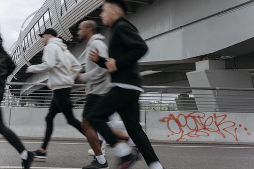 Free A group of people jogging briskly under an urban highway bridge showcasing graffiti and modern architecture. Stock Photo