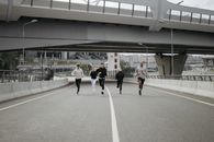一群不同背景的人在城市道路上奔跑，在立交桥下展现了团队合作与健身能力