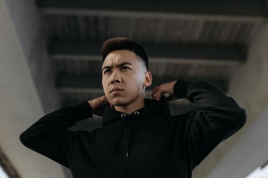 一名坚定的年轻人在城市桥梁下调整着黑色连帽衫的兜帽