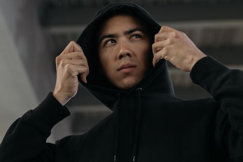 Free A young adult man in a black hoodie exuding confidence with a low angle shot indoors. Stock Photo