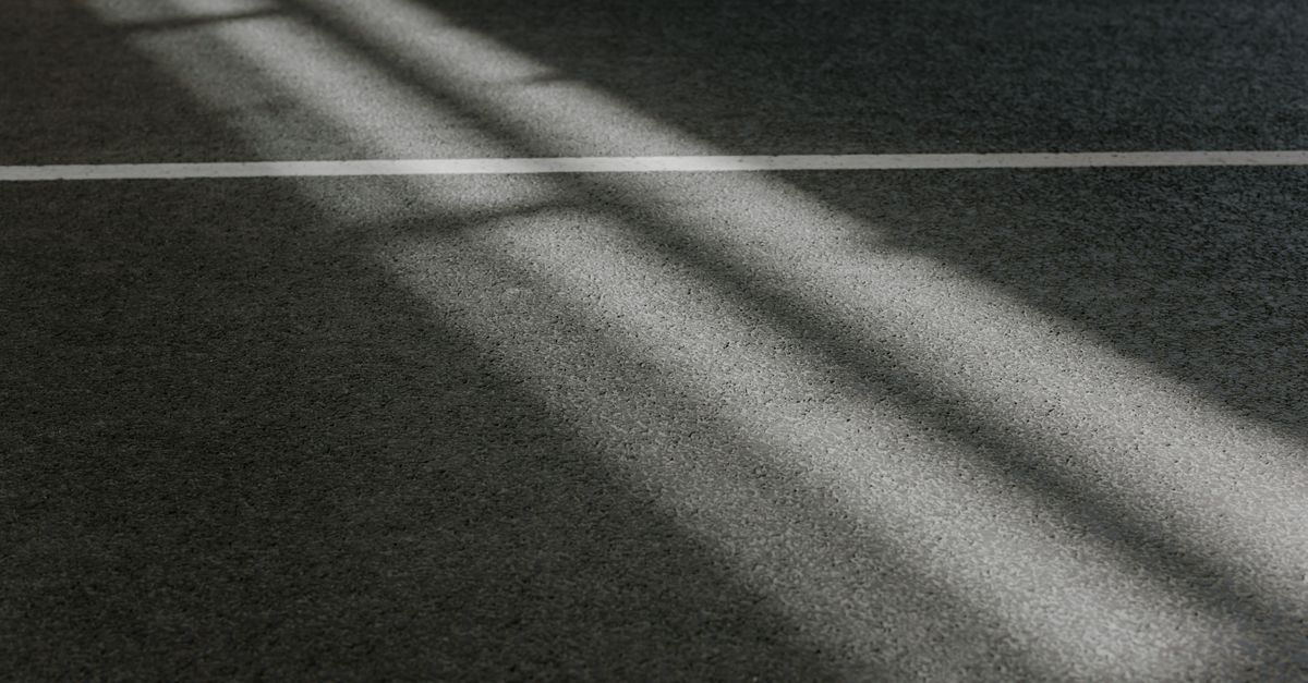Play of light and shadow on textured pavement surface with a single white line.