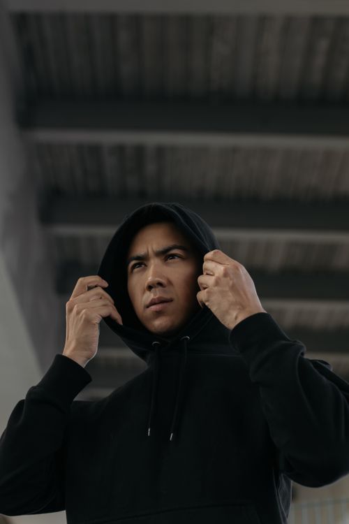 Free A focused young man adjusts his hoodie beneath a modern architectural structure. Stock Photo
