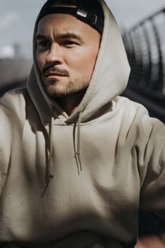 一名身穿米色连帽衫、帽子后戴的男子肖像，自然光映衬出他沉思的表情