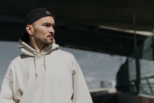 Free Young man wearing a hoodie and cap, looking away in an outdoor urban setting. Stock Photo