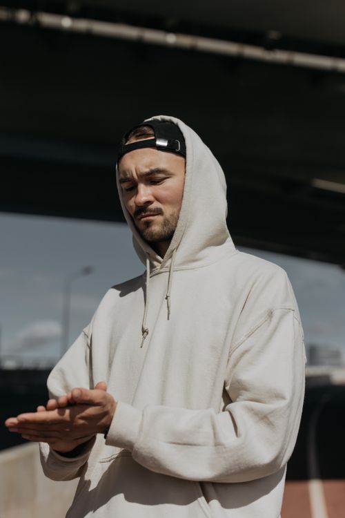 Free Man wearing a hoodie with a cap outdoors during the day. Urban casual style. Stock Photo