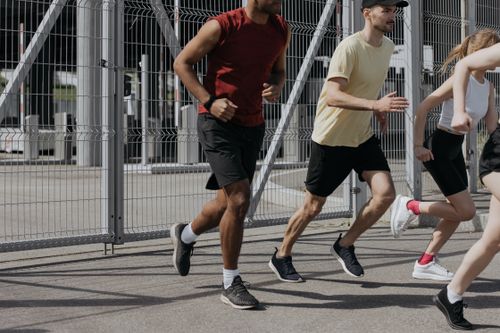 Free Energetic group of people running together outdoors under bright sunlight, wearing comfortable sportswear. Stock Photo