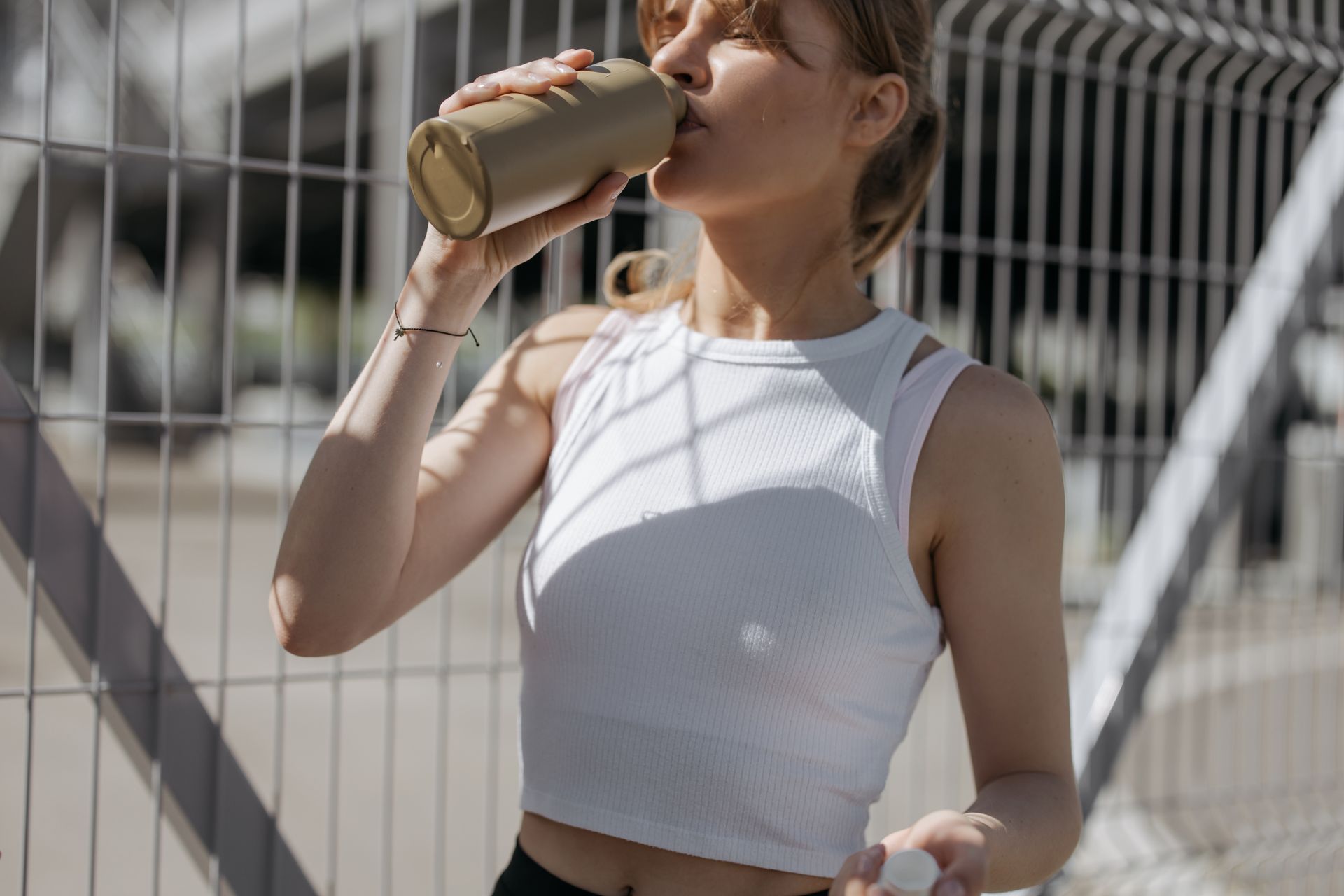 A Woman Wearing a White Tank Top Drinking from a Tumbler