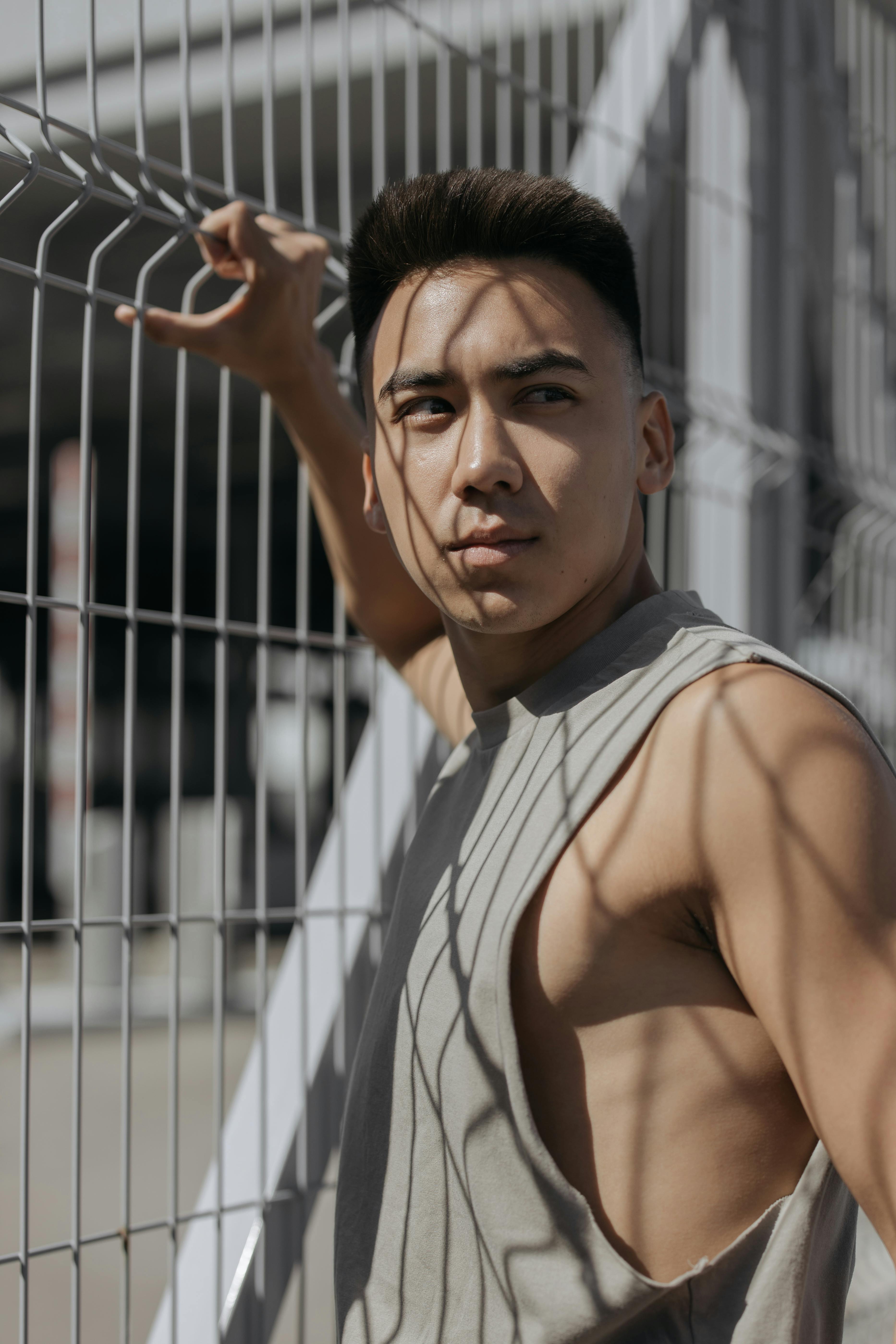 Portrait of a young man leaning on a metal fence, casting shadows outdoors.